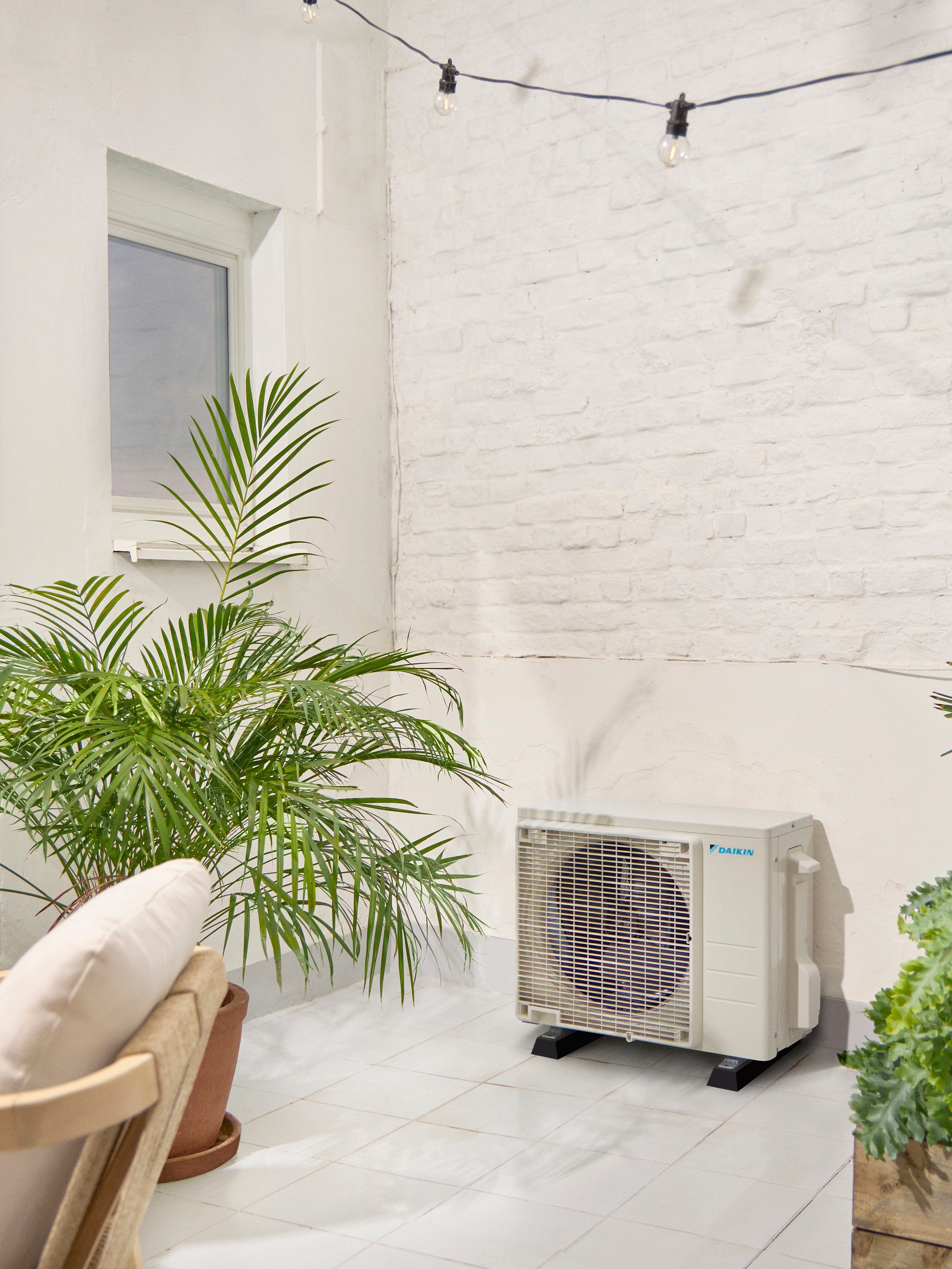 Daikin udendørsenhed på en hvid terrasse med en plante.